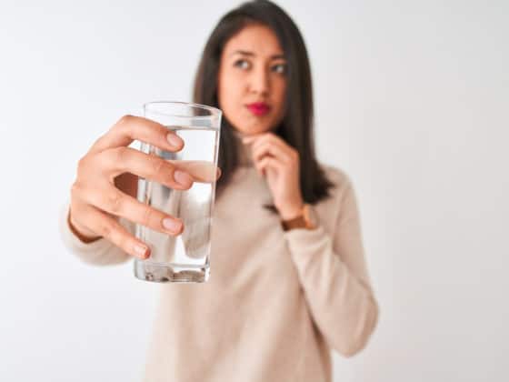 A woman with a thoughtful face holds a glass of distilled water.