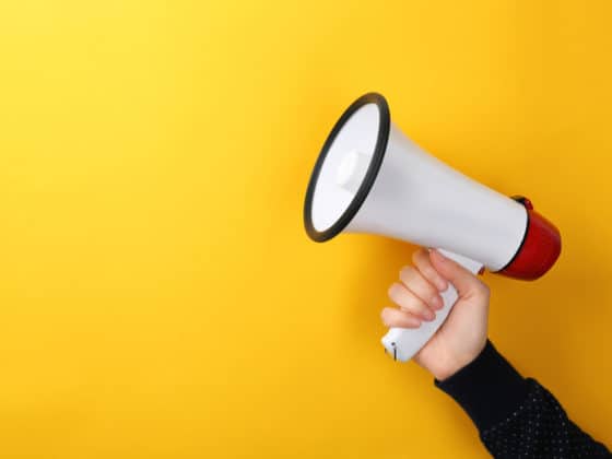A woman holding a white megaphone in front of a yellow background.