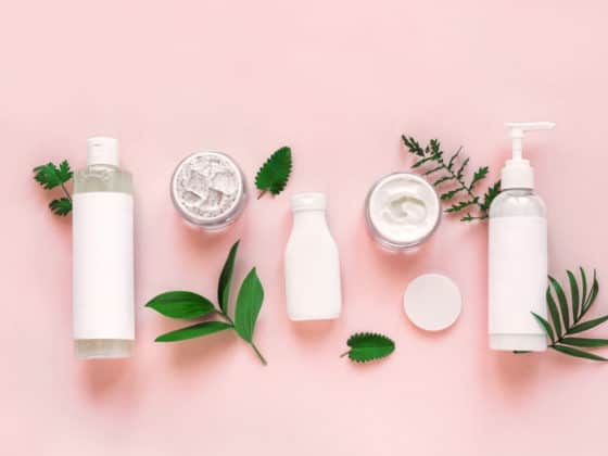White skincare bottles with green leaves on a light pink background.